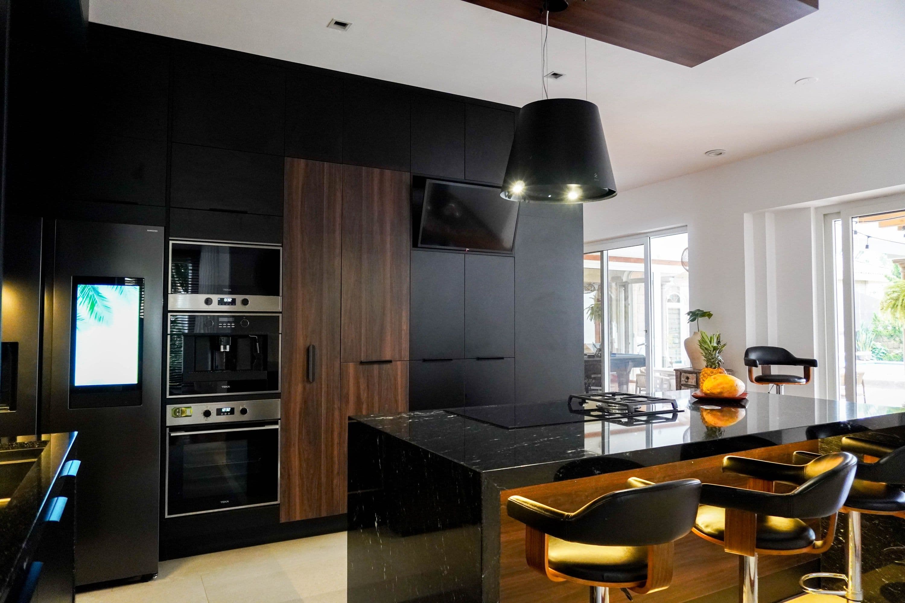 Remodelación de cocina y exterior Casa Villas, cocina negra con isla de mármol, electrodomésticos integrados y comedor.